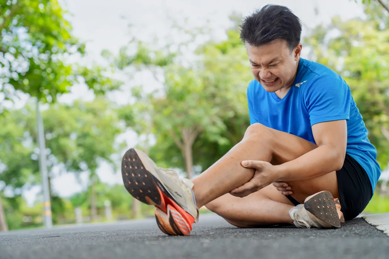 A runner sitting on a path holding a cramping calf