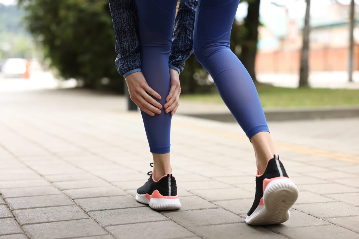 A woman on a pavement holding her calf
