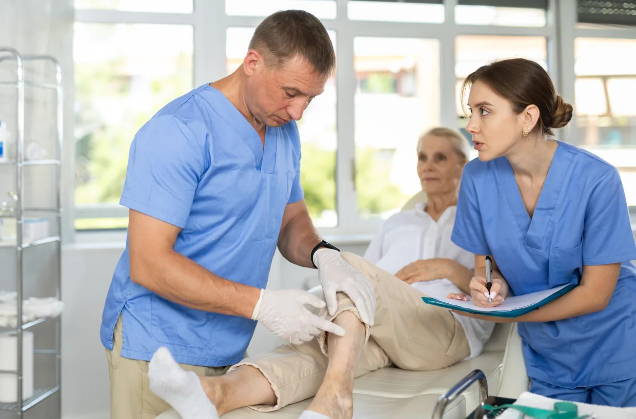 A clinician treating a patient leg while a colleague takes notes
